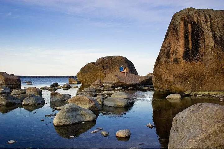 Person sitzt auf großen Findlingen am ruhigen Wasser des Lahemaa-Nationalparks.