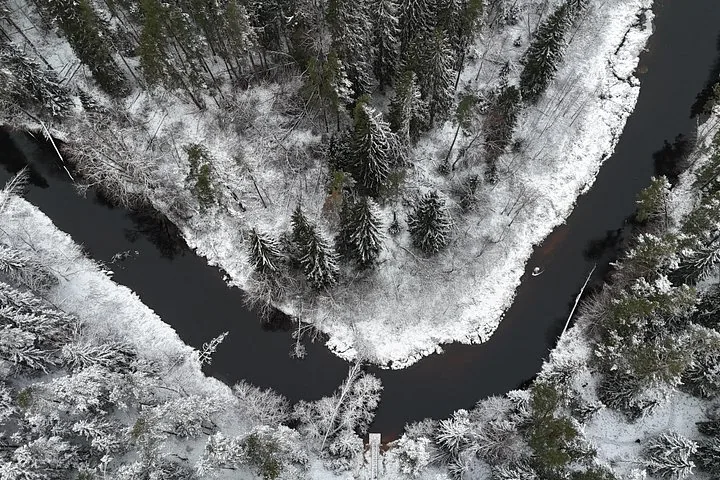 Luftaufnahme eines gewundenen Flusses, umgeben von verschneitem Wald.